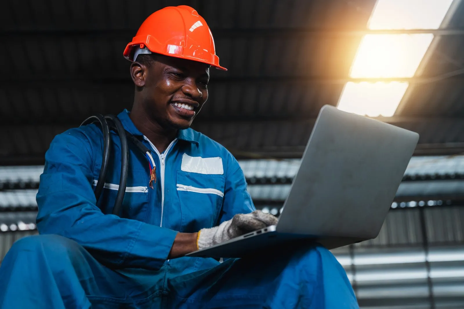 Engineer with a red hard hat and smiling at laptop